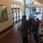 Kevin Holmes, KSHB; Brian Williams, Folly Theater; and Aubrey Morse, KSHB listening to Gale speak about Folly History in front of photocollage of the Folly's History.
